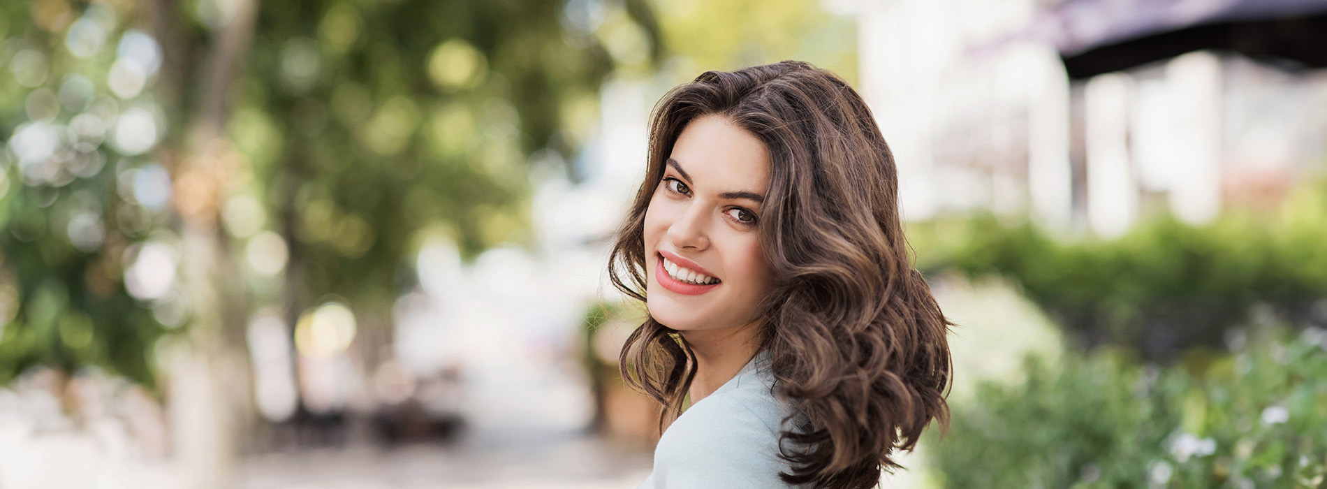Woman with long hair standing outdoors, smiling at the camera.