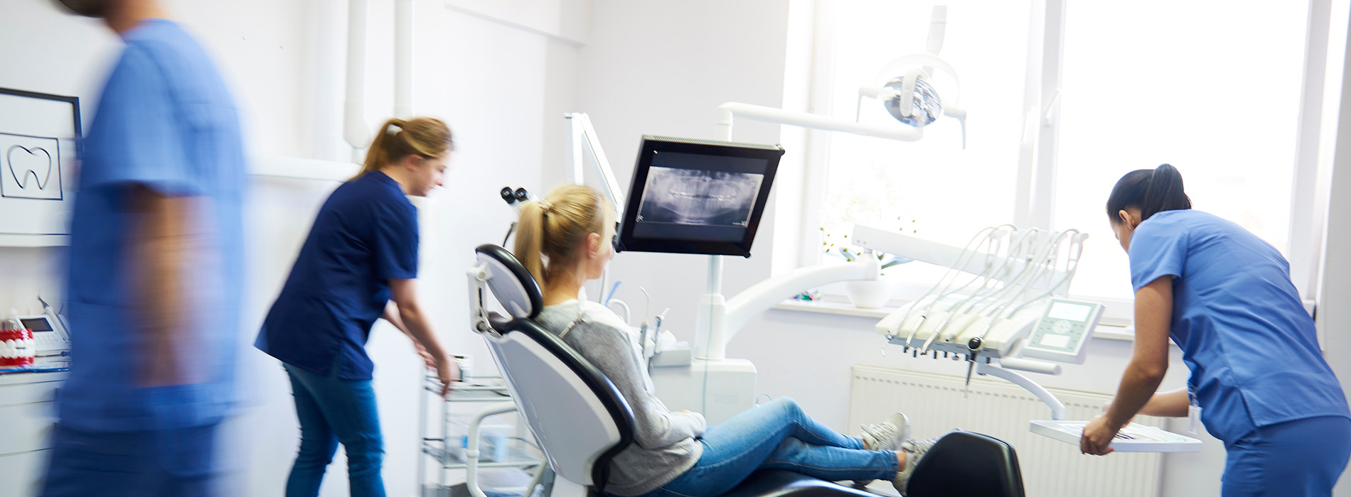 The image shows a bustling dental clinic with multiple professionals attending to their duties.