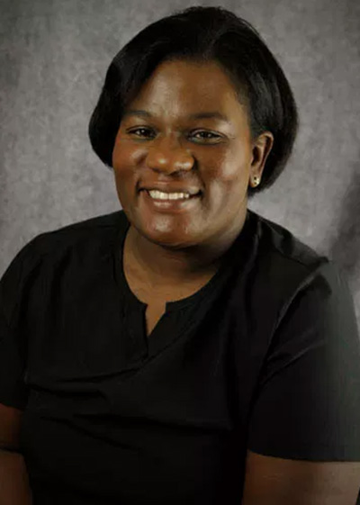 A woman with a smile, wearing a black shirt, poses against a grey background.