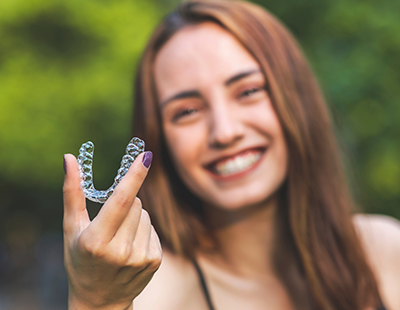A woman holding up a clear plastic mouthguard with a smile on her face.