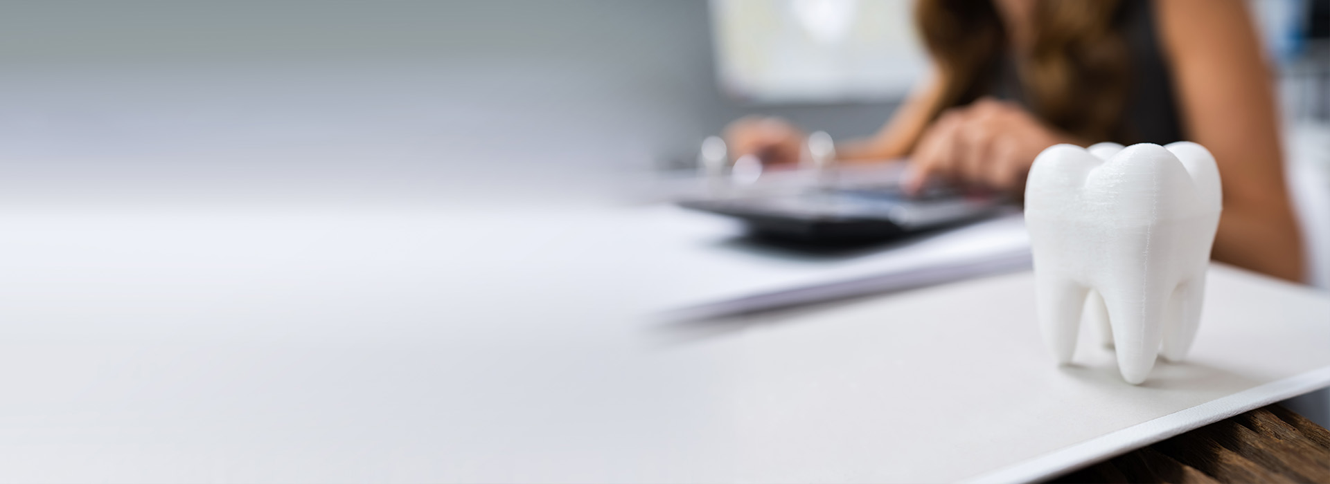 A person working at a desk with a computer monitor and a small white figurine of a tooth sitting on the desk.