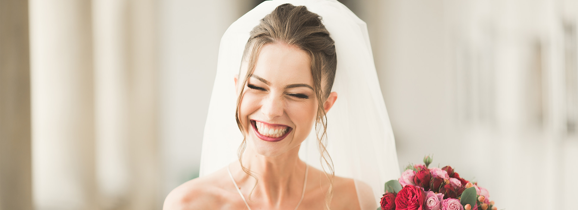 The image shows a bride wearing a white veil and holding flowers, smiling at the camera during her wedding ceremony.