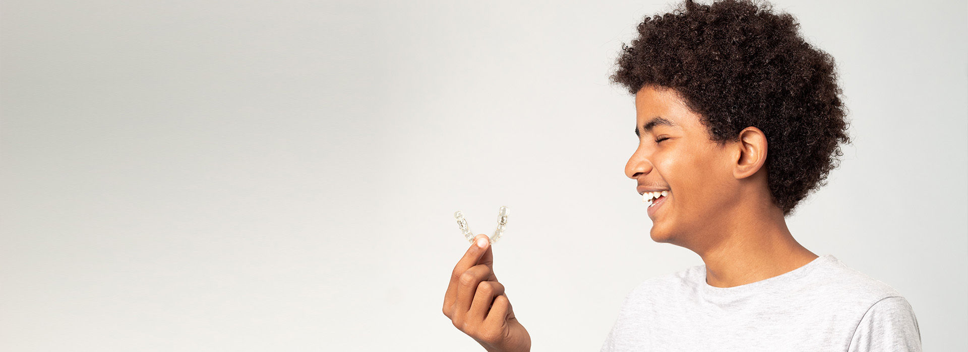A young boy with curly hair smiling and holding a small object in his hand.