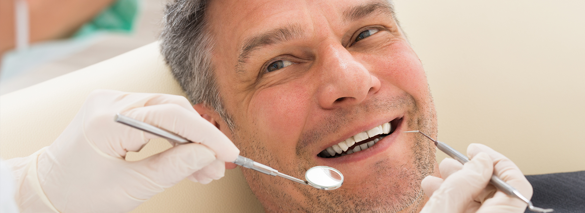 A man undergoing dental treatment, sitting in a dentist s chair with a smiling expression, while a dentist works on his teeth using dental tools.