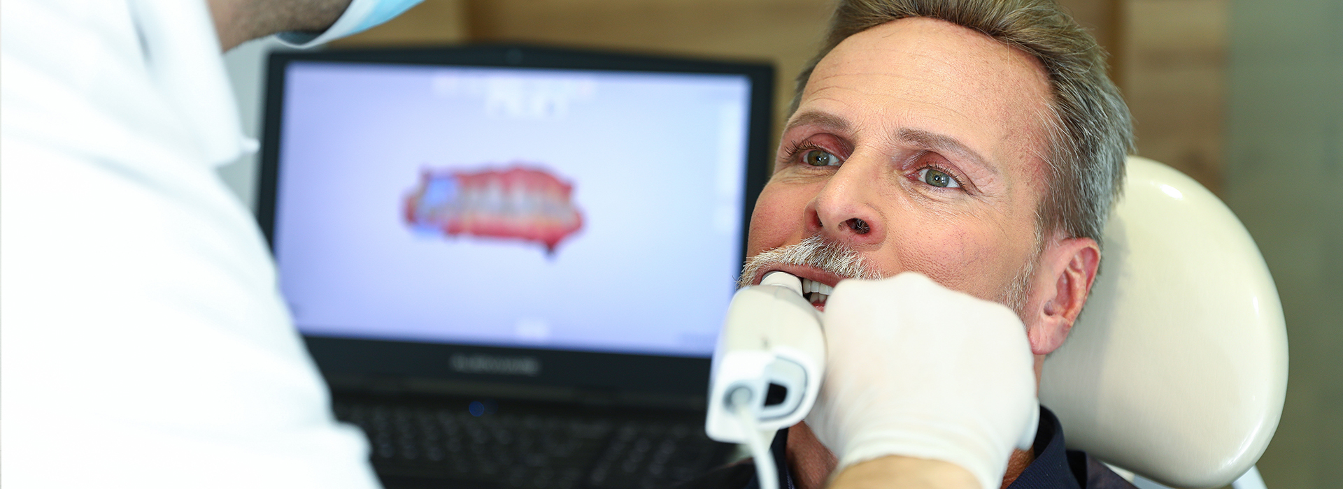 The image shows a man seated in a dental chair with his eyes closed, receiving treatment from a dentist who is operating on him while surrounded by medical equipment.