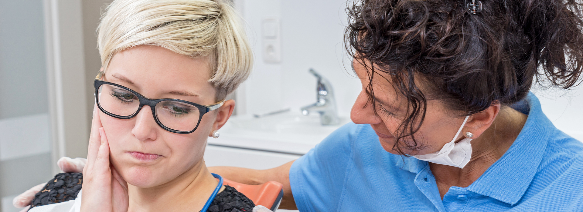 A woman with glasses is seated at a dental chair receiving oral care from a dentist.