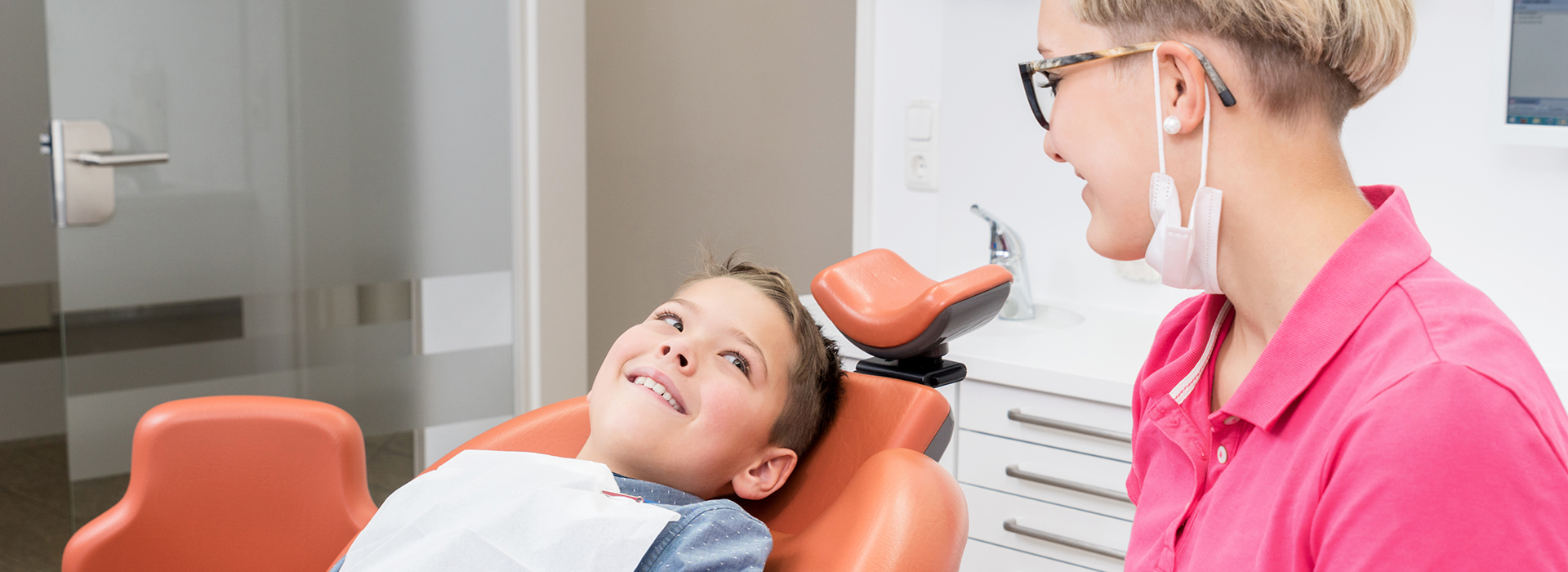 A person sitting in a dental chair smiling at the camera with a dentist standing behind them, both wearing face masks.