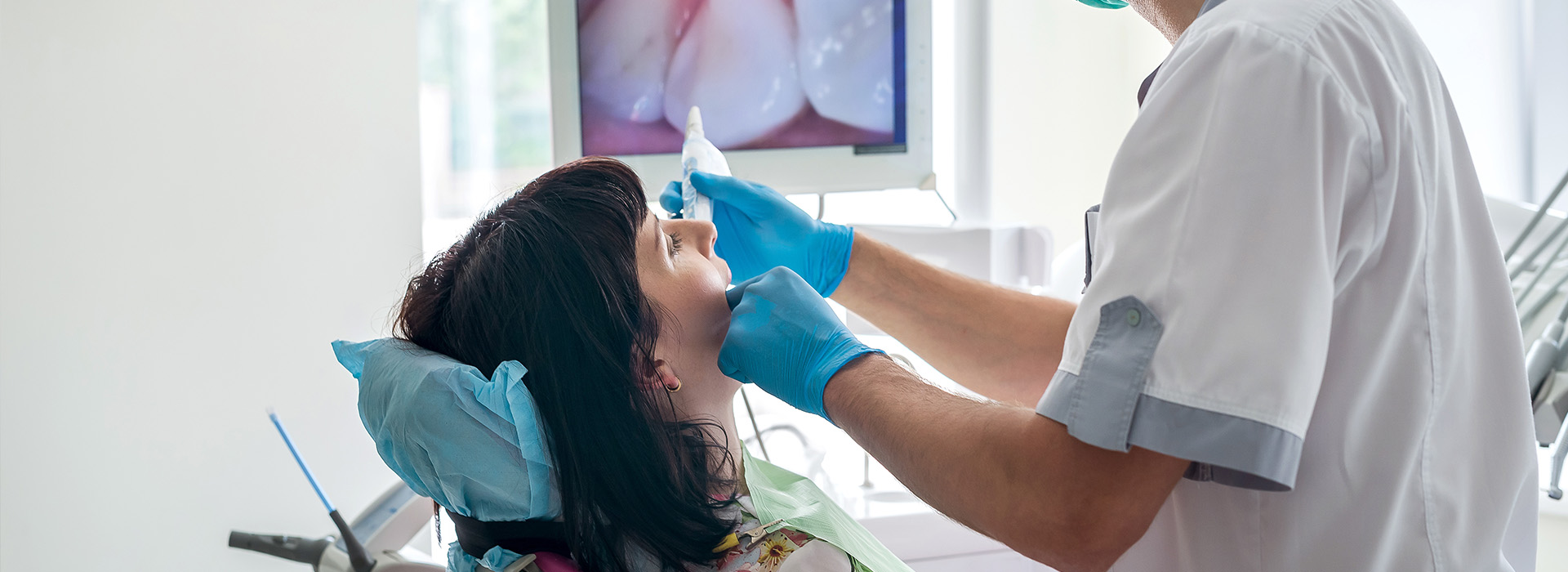 The image depicts a medical professional performing dental care on a patient, with the professional using a dental drill and wearing protective eyewear.