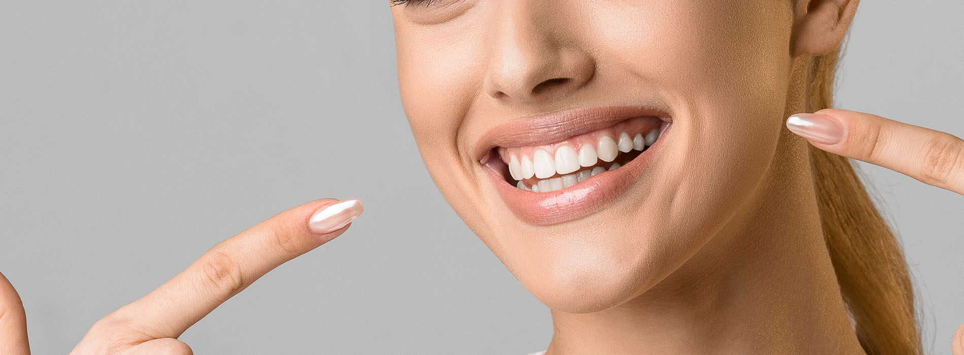 A woman with a bright smile holds up two fingers, showing a perfect set of teeth, against a white background.