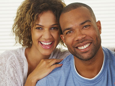 A man and woman posing together, with the man smiling and wearing a white t-shirt, and the woman smiling and wearing a dark top.