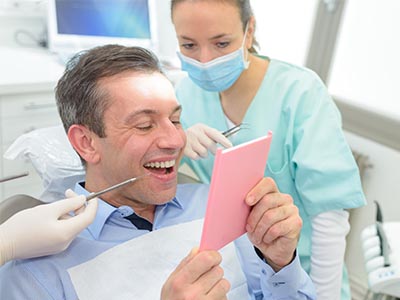 Man in dental chair holding up pink card with surprised expression while dental professional looks on.