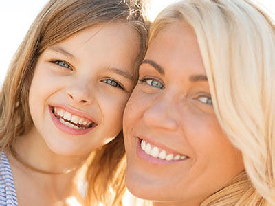 The image depicts a woman and a young girl smiling at the camera with a blurred background.