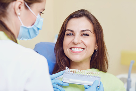A woman with a smile sitting in a dental chair while a dental professional checks her teeth.