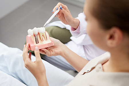 The image shows a person holding a pink dental model with a tooth missing, while another individual appears to be examining or demonstrating something related to oral health care, likely within a dental clinic setting.