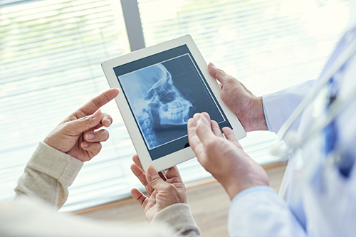 The image shows two people holding tablets displaying an X-ray, with a medical professional standing behind them, examining the screens alongside them.