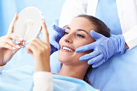 Woman lying on dental chair with magnifying mirror held over her face by medical professional.