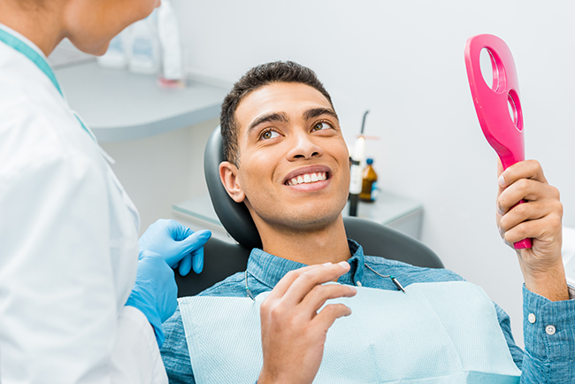 A man sitting in a dental chair with a smile on his face, receiving dental care from a professional.