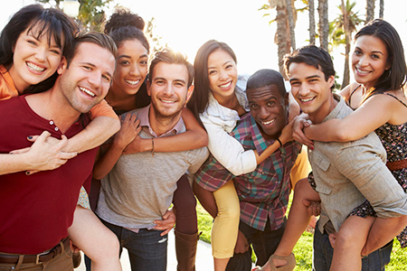 The image depicts a group of young adults posing together outdoors, smiling and embracing each other.