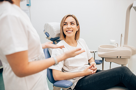 A woman sitting on a dental chair with a smile, while a dental professional stands behind her holding her hand.