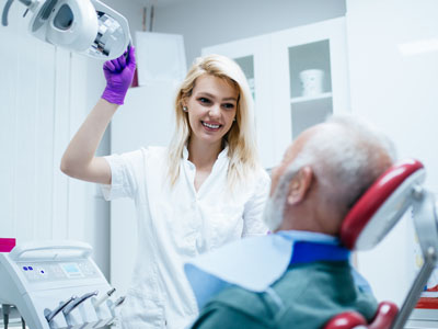 A female dental hygienist assisting an elderly patient during a dental appointment.
