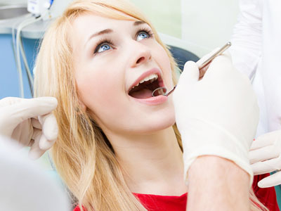 The image displays a young woman seated in a dental chair, receiving dental treatment with a dentist performing the procedure.