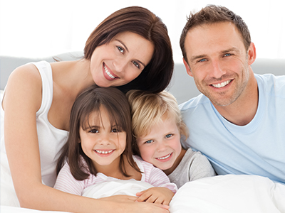 A family of four adults and two children posing together on a bed with happy expressions.